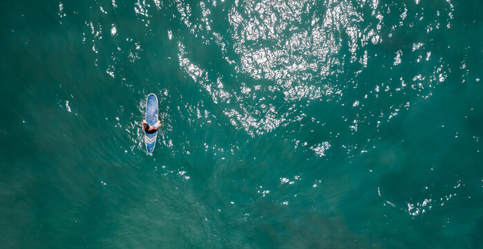 aerial top down view of surfer whith surf board in ocean wave from drone 
