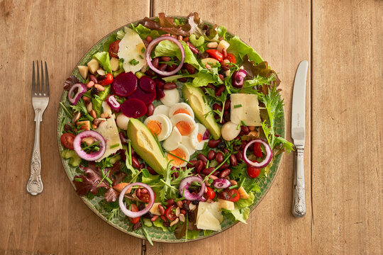 Green plate of healthy salad with knife and fork