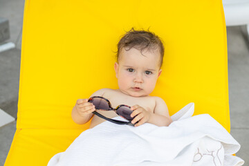 toddler is relaxing sitting on plastic folding lounge beach chair with yellow color mattress.baby...