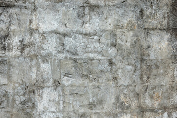 Fragment of an old gray plastered wall. Through the surface, covered with irregularities and cracks, stone blocks appear. Grunge. Background. Texture.