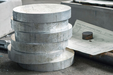 Aluminum round timber cut into blanks for processing on lathes. Aluminum blanks with blueprints on...