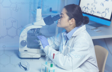 Serious young mixed race doctor of chemistry in lab coat sitting at desk and studying molecular...