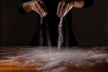 Mão derrubando farinha branca de trigo sobre a mesa com fundo preto