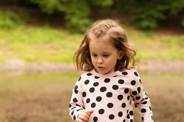 little beautiful red-haired girl runs in a polka-dot dress in a summer park