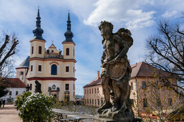 Fototapeta na wymiar Litomysl, Czech Republic, 17 April 2022: Church of the Finding of the Holy Cross and Piarist dormitory near castle, Regional Museum baroque building with tower at sunny summer day, stone statues