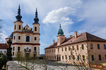 Fototapeta na wymiar Litomysl, Czech Republic, 17 April 2022: Church of the Finding of the Holy Cross and Piarist dormitory near castle, Regional Museum baroque building with tower at sunny summer day, stone statues