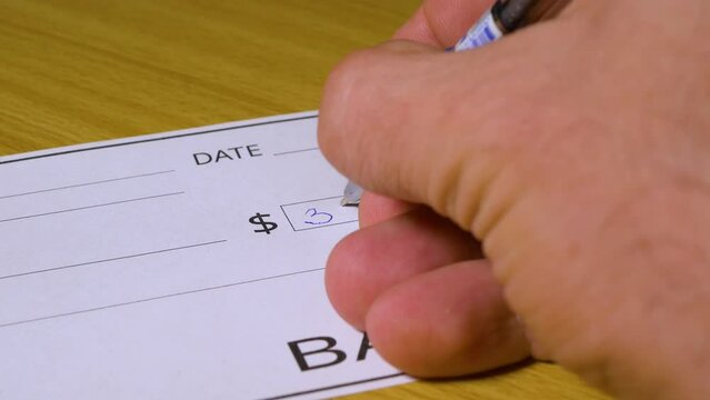 A man writes a bank check for three thousand dollars, close-up, selective focus