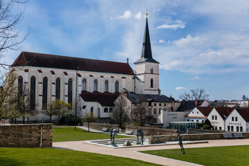Fototapeta na wymiar Litomysl, Czech Republic, 17 April 2022: gothic medieval church of the Exaltation of the Holy Cross with tower at sunny summer day, Fountain in Monastery Garden, stone statues