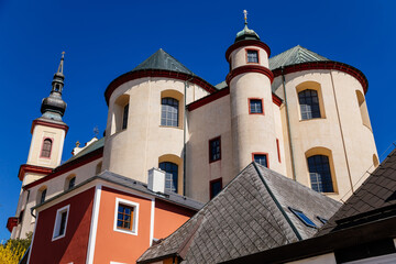 Litomysl, Czech Republic, 17 April 2022: Church of the Finding of the Holy Cross and Piarist dormitory near castle, baroque building with tower at sunny summer day, stone statues in the garden