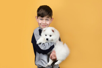 Handsome young boy happily holds his little white dog in his arms and plays with her, dog and boy...