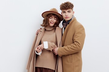 a sweet, beautiful, loving couple stands on a white background in stylish beige autumn clothes, gently cuddling up to each other and the woman smiles happily