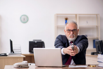 Old businessman holding gun at workplace