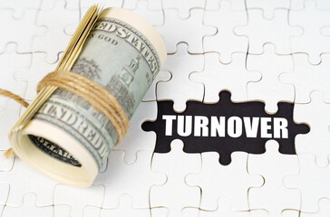 Dollars lie on white puzzles, on a black surface there is an inscription - Turnover