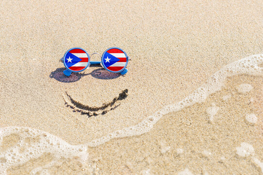 A painted smile on the beach and sunglasses with the flag of the Puerto Rico. The concept of a positive holiday in the resort of the Puerto Rico.