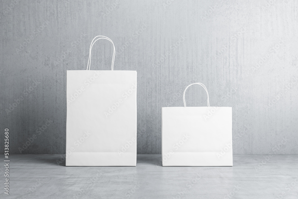 Poster front view on two blank white paper shopping bags with place for your logo or text on concrete floor