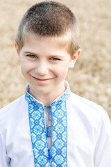 Portrait of schoolboy boy in traditional embroidered Ukrainian shirt on background of wheat field on sunny day. Blue embroidery. Child is sincerely smiling. Independence Day, Constitution of Ukraine.