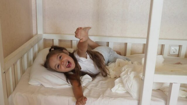 little girl at home in bed in pajamas, with long hair, ponytails. doesn't want to sleep, plays around. time before bed. good night. kicks the blanket. family before bed