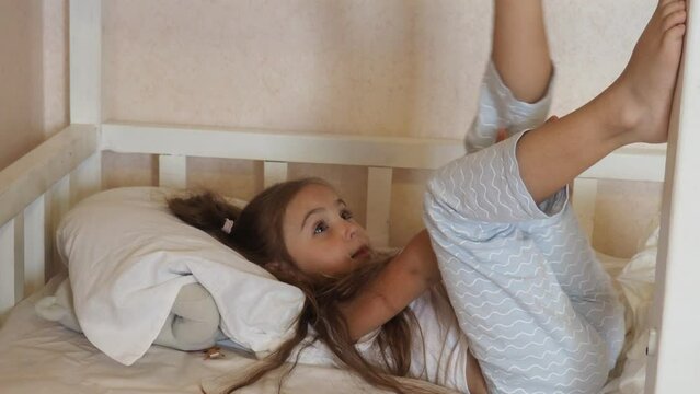 little girl at home in bed in pajamas, with long hair, ponytails. doesn't want to sleep, plays around. time before bed. good night. kicks the blanket. family before bed