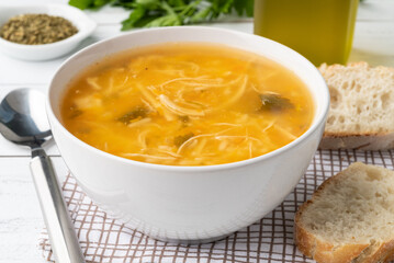Chicken soup in a bowl with bread slices and seasoning over wooden table