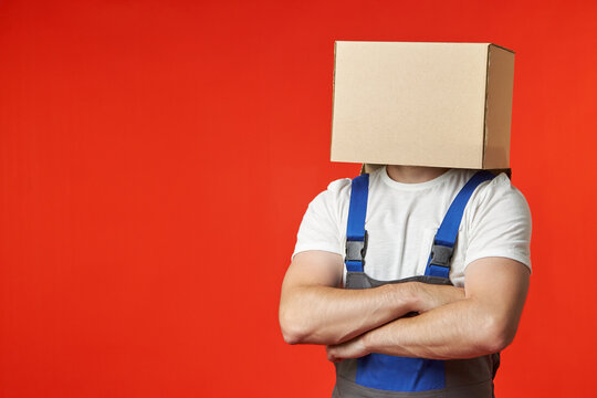 Anonymous loader confidently stands in a work suit with straps on a red background with a box on his head. A professional male loader thinks only about the safety and security of the transported items