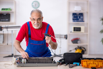 Old repairman repairing air-conditioner at workshop