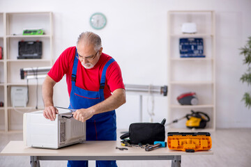 Old repairman repairing oven at workshop
