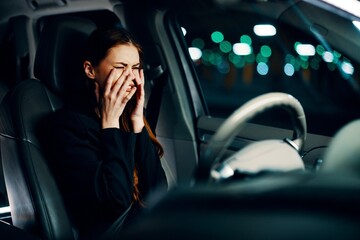 a frustrated, emotional, crying woman is sitting behind the wheel of a car with her seat belt fastened, crying, covering her face with her hands. Photography at night