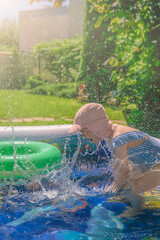 Little girl splashing in a pool on a sunny day. Summer concept. Kid playing in pool, hot summer day in back yard. Summer water games.
