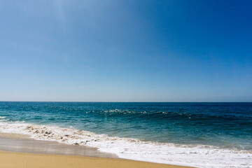 Fototapeta na wymiar Ocean seascape with waves washing up onto sandy beach under a clear blue sky 