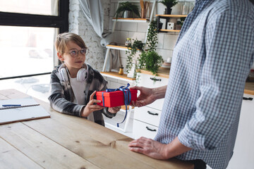 Handsome young father giving a birthday present in a red box to his teenager son. Boy receives bright red box for his anniversary.