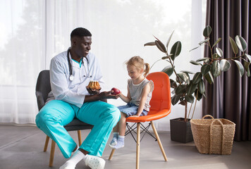 Fototapeta premium an African-American nutritionist communicates with a small patient and offers a fresh apple