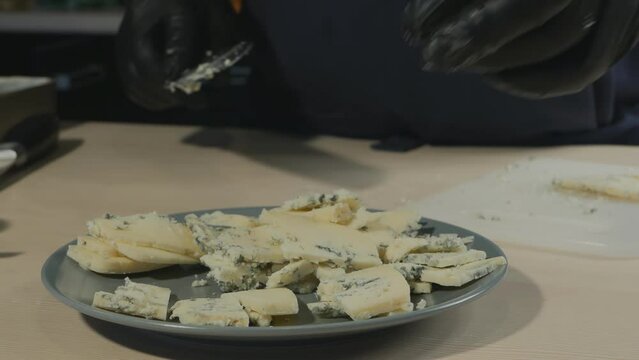 pastry chef with a large knife cut cheese with mold dorblu into a bowl. Important ingredient in dessert