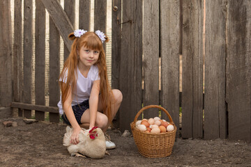 A little girl on summer vacation in the village feeds chickens and collects eggs on a farm