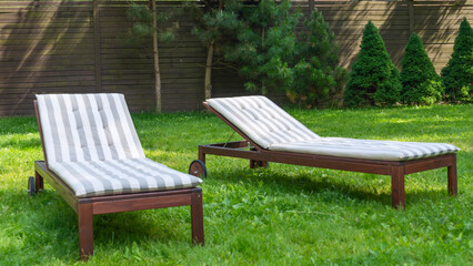 Lounge chairs on the backyard in a beautiful garden. Two empty sunbeds on the grass.