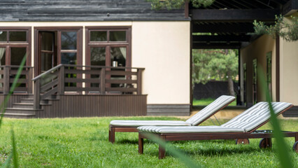 Lounge chairs on the backyard in a beautiful garden. Two empty sunbeds on the grass.