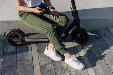 Young woman in white sneakers is sitting on electric scooter