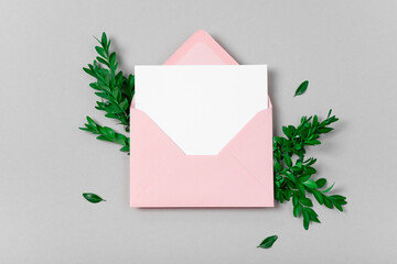 Real photo. Pink envelope square invitation white greeting card mockup with a boxwood branch. Top view with copy space, pastel grey background. Template for branding and advertising