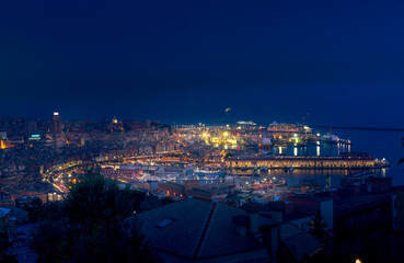 Night cityscape of Genova with the old port, cruise ships, sea and port cranes in the background