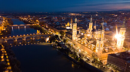 Fototapeta na wymiar Scenic twilight view from drone of illuminated Basilica of Our Lady of Pillar on bank of Ebro river in Spanish city of Zaragoza ..