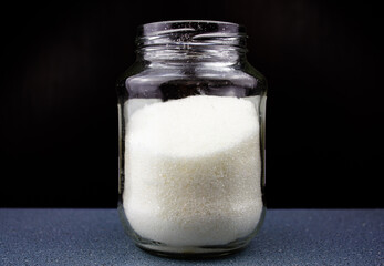 Sugar in a glass jar on a black background. Sugar crumbs in a glass jar.
