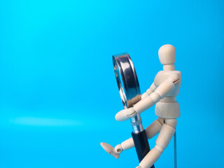 Wooden mannequin holding magnifying glass on a blue background with copy space.