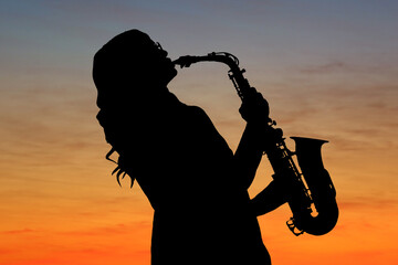Silhouette of woman playing saxophone against beautiful sky at sunset