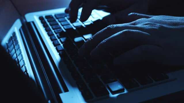 暗い部屋でパソコンのキーボードを打つ男性の手のクローズアップ