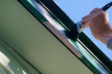 A top coat of paint is being applied to a barge board, the dark green will cover the pink undercoat or primer