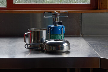 A stainless steel mug, portable kettle and gas stove are waiting to be used to prepare the evening meal.