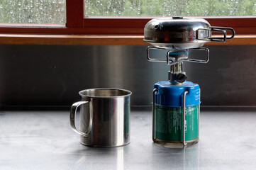 A well deserved cup of tea is being prepared at the end of a days hiking or tramping, the kettle is nearly boiling on the small gas stove, the stainless steel mug is ready