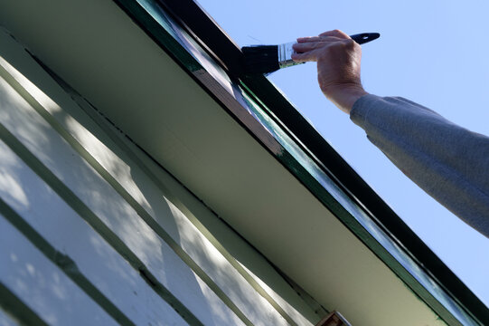 A person is painting a green house, they are covering up the undercoat
