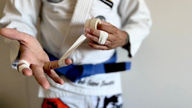 A male brazilian jiu-jitsu athlete is getting ready to train by taping his fingers.
