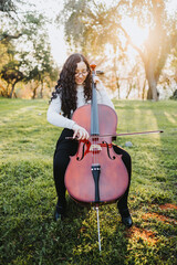 Young brunette woman with glasses playing cello at sunset in the park, on a green grass. Vertical © padnob