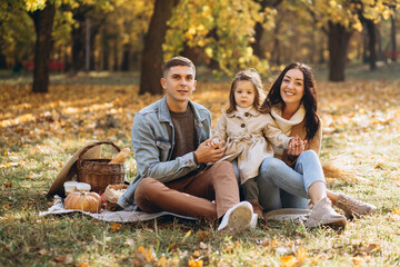 Fototapeta premium Portrait of happy young family sitting on plaid together in autumn park